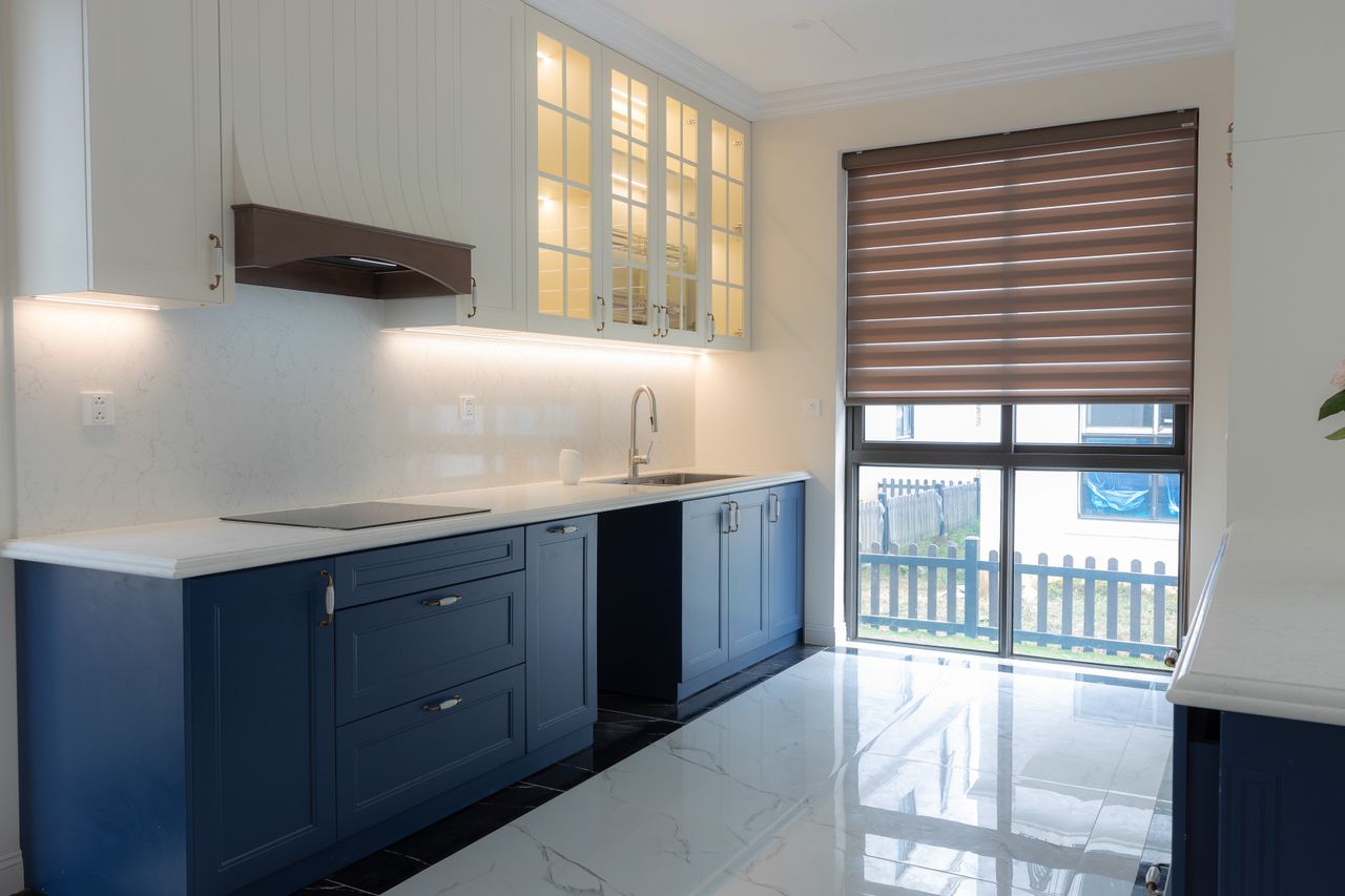 our-stories Bright modern kitchen featuring blue cabinetry, marble countertops, and ample natural light through large windows.