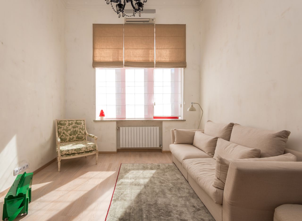 Bright, minimalist living room with beige sofa and classic armchair under warm natural light.